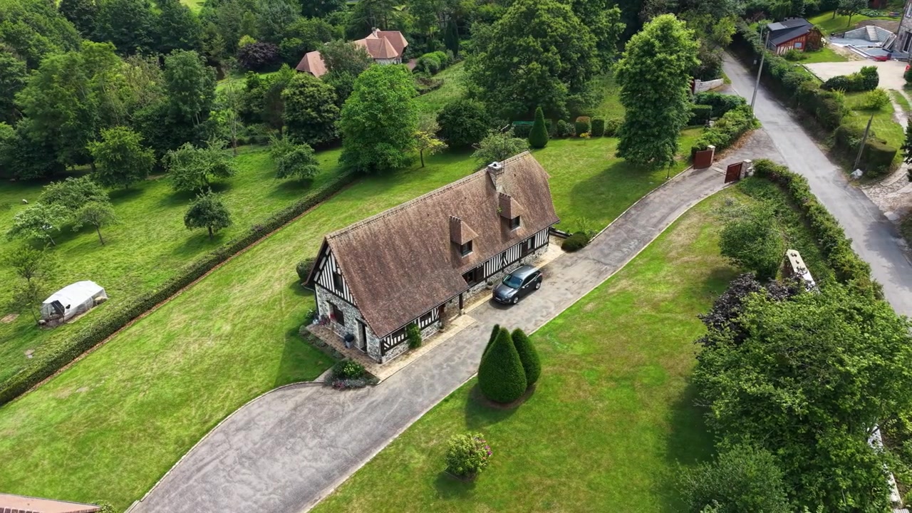 Drone view of a traditional thatched-roof cottage surrounded by gardens, trees, and green countryside near Honfleur, Normandy, France