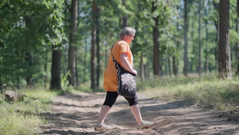 Cinematic-shot-of-Fat-woman-with-Orange-T-shirt-crossing-the-path-in-green-Forest-looking-for-mushrooms-in-grass-in-slow-motion-during-sunny-day