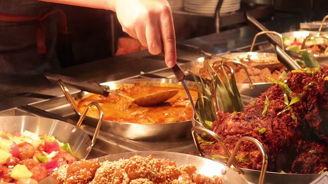 Uno chef usa le pinze e i cucchiai per servire curry e pollo fritto su un piatto