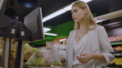 Middle-aged-woman-weighs-a-bag-of-apples-in-the-supermarket