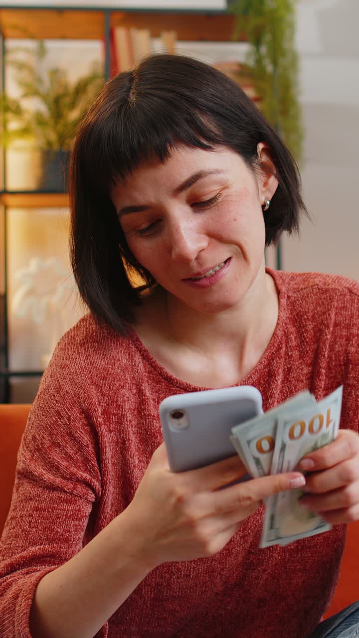 Donna che conta denaro banconote in dollari risparmio guadagni usando la calcolatrice dello smartphone sul divano a casa