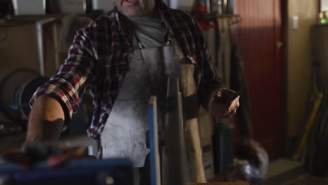 caucasian male knife maker in workshop wearing glasses and using sander