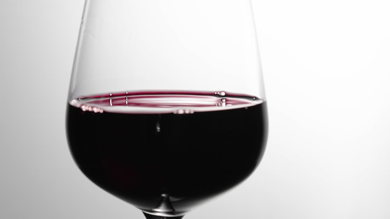 el vino tinto se asienta después de ser arremolinado en una copa de vino a cámara lenta, con fondo blanco