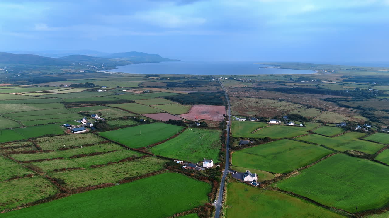 Vast green valley divided into the fields used for farming. Waterscape surrounded by the mountains and plain at backdrop. Ireland scenery from top.