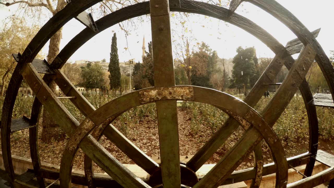 el molino de agua se mueve en el canal cerca de la piscina de peces sagrados el agua fluye en el fondo árboles verdes y amarillos urfa