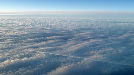 incredible view from the cockpit of an airplane flying high above the clouds leaving a long white condensation vapour air trail in the blue sky