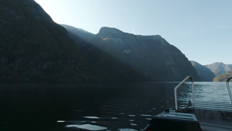 un bote de costillas se desliza suavemente sobre un fiordo en noruega hacia los rayos de sol que pasan sobre la cima de una montaña
