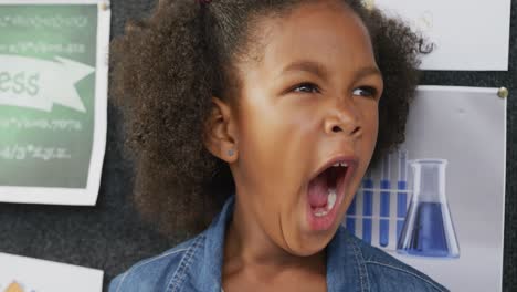 video portrait of happy, tired biracial schoolgirl yawning in school classroom