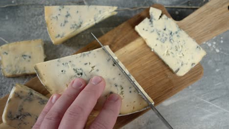 male hand cut pieces of brie cheese on a cutting board.