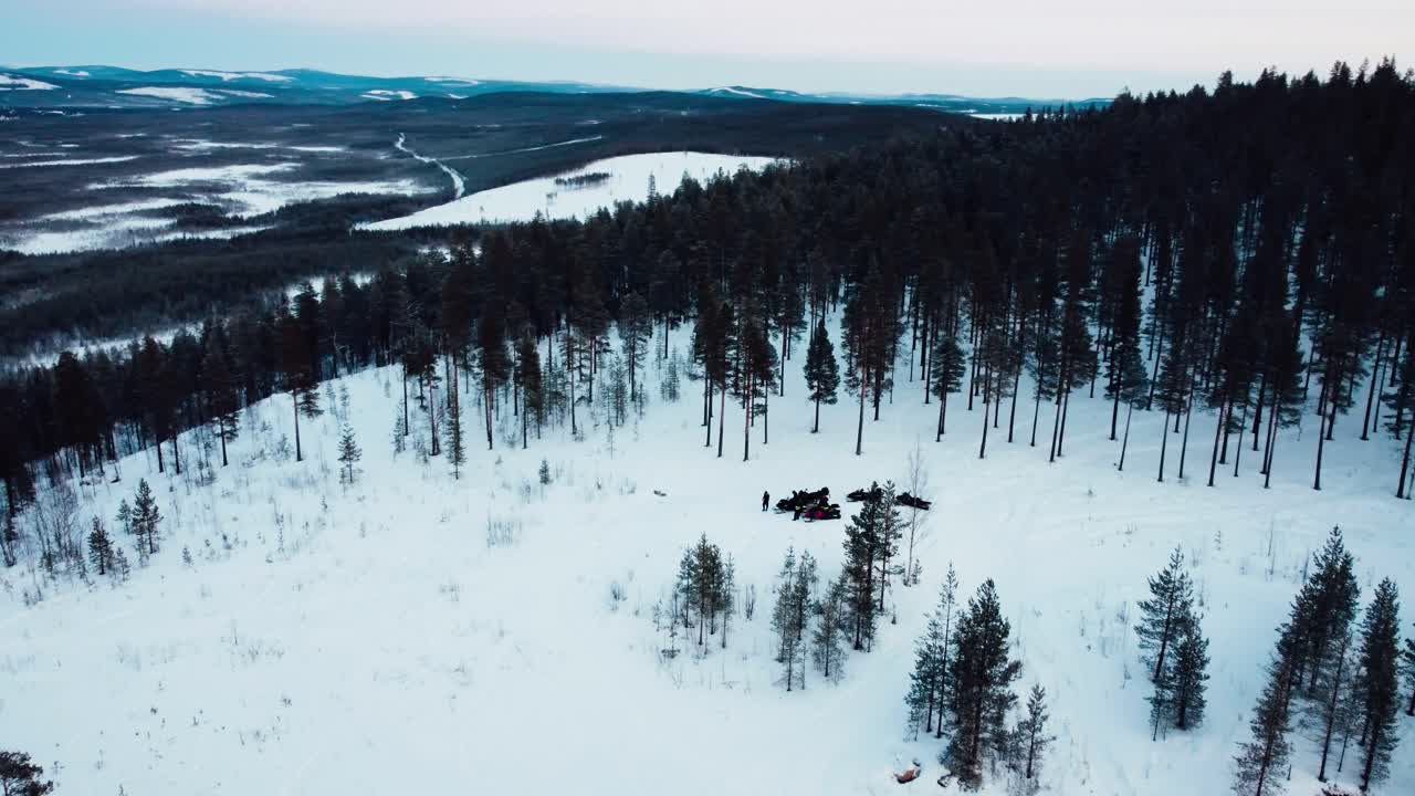 disparo de drone de un grupo de personas paradas en la cima de una montaña con motos de nieve durante la puesta de sol desde la distancia con una hermosa vista