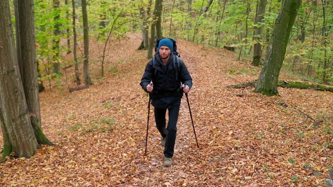 Nuori mies vaeltamassa vaellussauvojen kanssa syksyisessä metsässä
