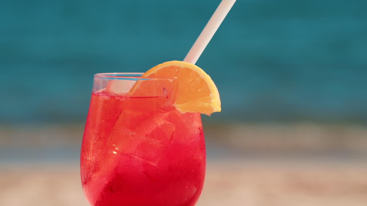Refreshing red orange cocktail with ice and orange slice against the deep blue Mediterranean Sea