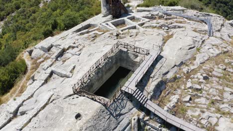 Drohne-Umkreist-Und-Zieht-Sich-Langsam-Zurück,-Während-Sie-Einen-Mit-Stahlgeländern-Umschlossenen-Wasserbehälter-Und-Eine-Plattform-In-Der-Antiken-Stadt-Perperikon-In-Der-Provinz-Kardschali-In-Bulgarien-Zeigt