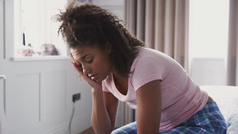 woman wearing pajamas suffering with depression sitting on bed at home