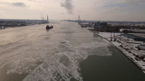 Cargo-vessel-transports-goods-on-icy-river-of-Detroit-with-cityscape-in-both-sides