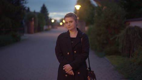 cute girl standing in a coat under the lights of lamps on an autumn evening in the city