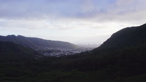 Drohnenaufnahmen,-Die-Zwischen-Zwei-üppigen-Grünen-Bergen-Hindurchführen-Und-Eine-Stadt-Dazwischen-Offenbaren,-Mit-Einer-Silhouette-Der-Stadt-Honolulu-Am-Horizont-Im-Nebel