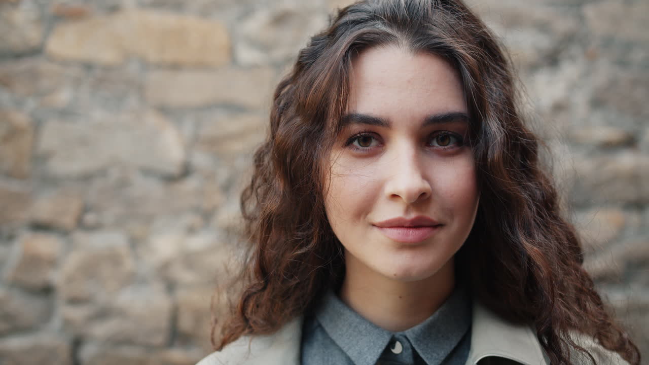 Woman with curly hair smiling in front of a stone wall