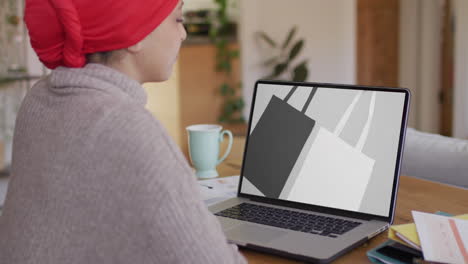 mujer biracial en la mesa usando portátil, compras en línea para bolsas, cámara lenta
