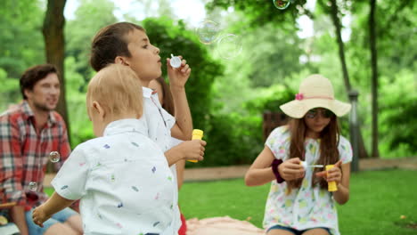 children blowing bubbles outdoors. parents spending time with kids in park