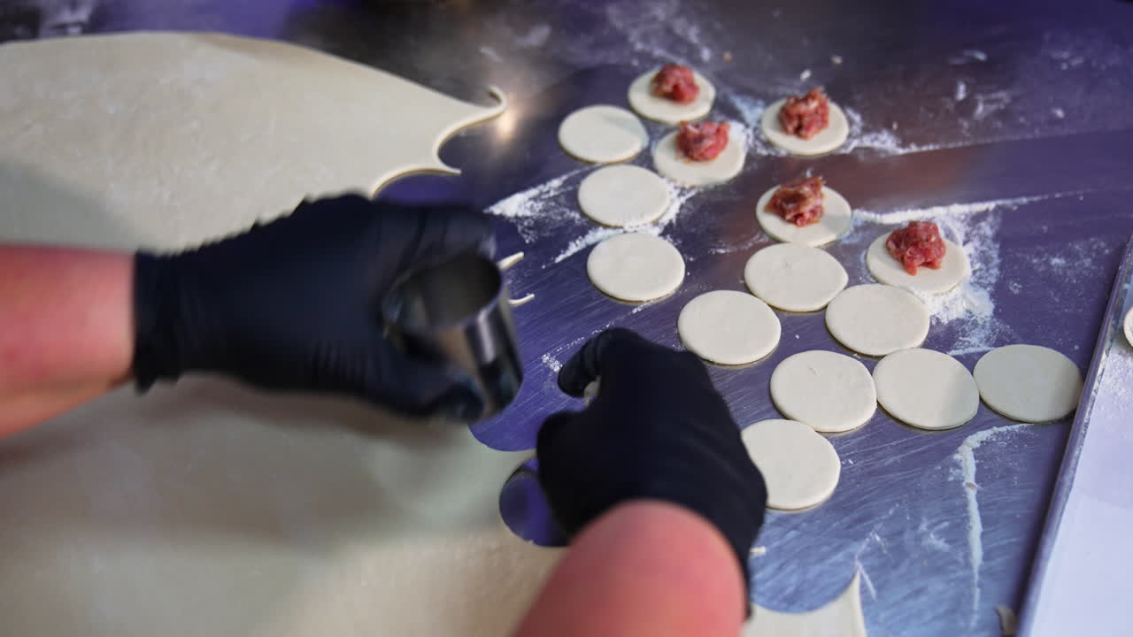 Hands in black latex gloves cut the little circles from duff. Worker lays the minced meat on top of the circles. Close up.