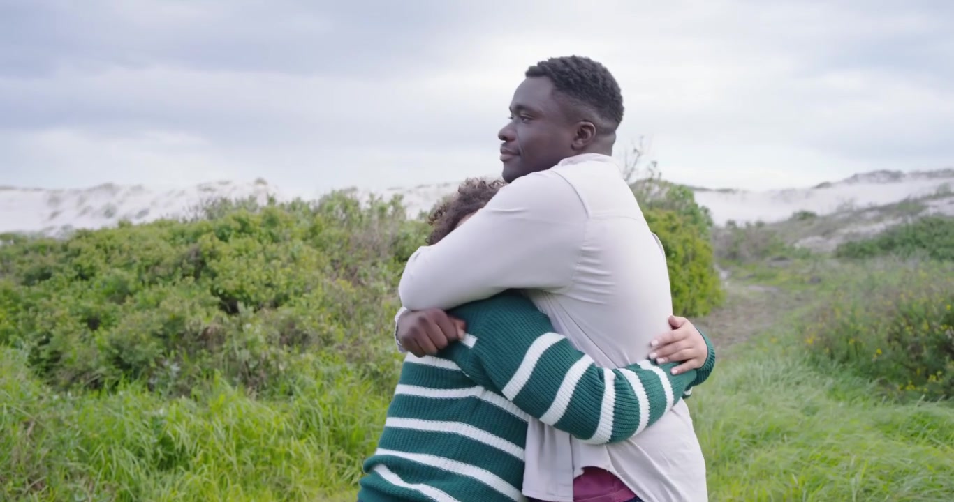 Couple walking grassy path, holding hands, striped sweater partner pointing, leading to embracing