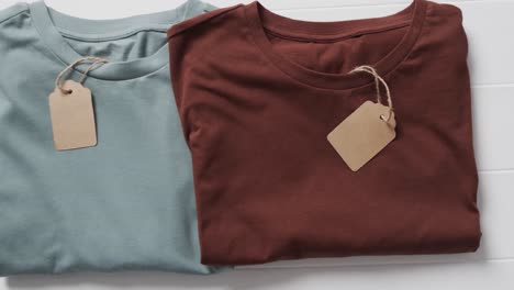 video of flat lay of multi coloured t shirts with tags and copy space on white background