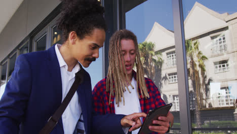 Two diverse male friends walking in the street using a digital tablet