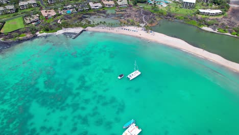 sailboats anchored in the anaehoomalu bay not far from the white sand beach - aerial pull back reveal