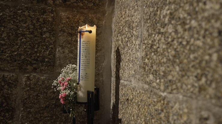 burning candle with handwritten prayer beside baby’s breath and pink flowers on stone wall