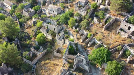 Luftaufnahme-Von-Oben-Nach-Unten-Auf-Das-Verlassene-Geisterdorf-Kayakoy-In-Fethiye,-Türkei,-An-Einem-Sonnigen-Tag,-An-Dem-Nur-Noch-Ruinen-übrig-Sind,-Umgeben-Von-überwucherten-Bäumen