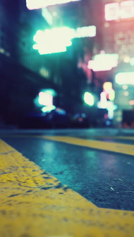 a blurry view of a city street at night, with neon lights and a yellow crosswalk in the foreground.