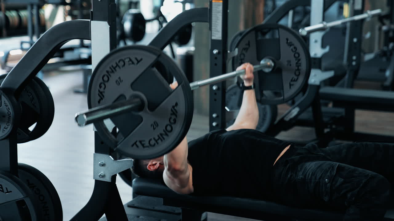 Bodybuilder Doing Barbell Exercise. Young man flexing muscles with barbell in the gym