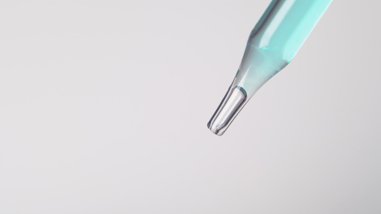 punta de gotero de pipeta con goteo de líquido azul claro en fondo blanco