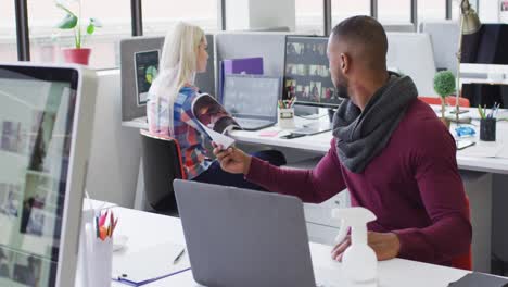 Mixed-race-businessman-using-laptop-going-through-paperwork-in-modern-office