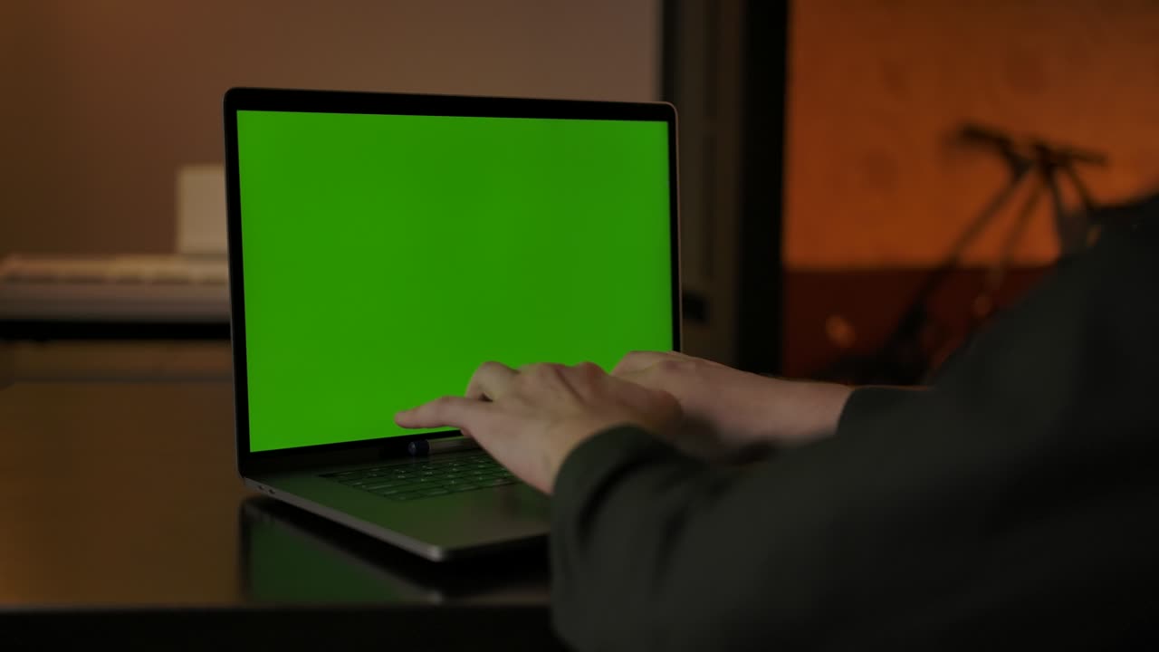 un hombre sin rostro escribiendo algo en el teclado de una computadora portátil de pantalla verde