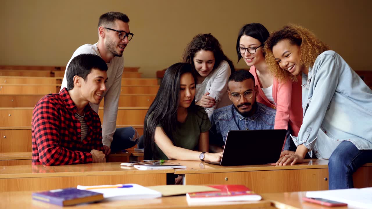 un equipo multirracial de estudiantes está trabajando con una computadora portátil escribiendo y mirando la pantalla, los jóvenes están discutiendo el proyecto y sonriendo. trabajo en equipo y concepto de tecnología.