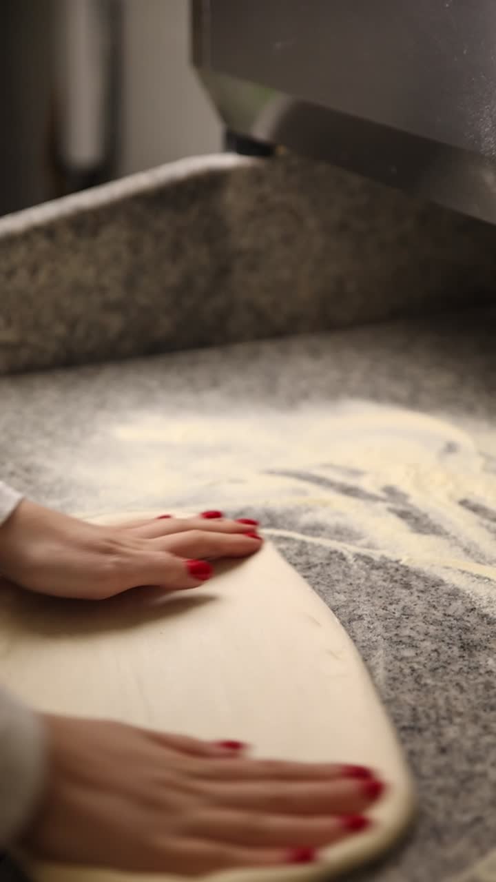 Primo piano di mani che premono l'impasto della pizza su un piano di lavoro infarinato