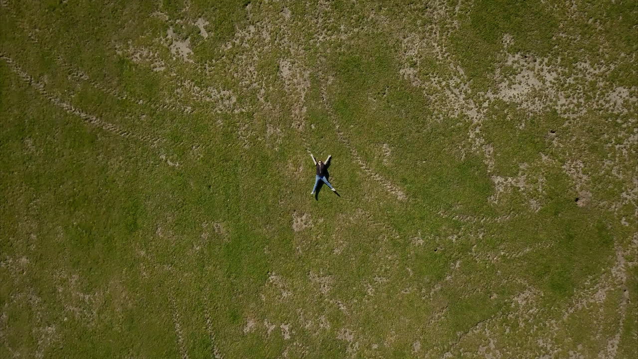 공원의 푸른 잔디에 누워 있는 검은색 티셔츠를 입은 성인 여성 위로 날아가는 공중 드론 샷