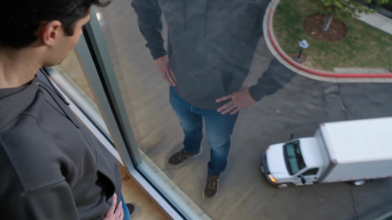 Watching man in hoodie leaning at home by large glass, studying reflection while truck pulling in