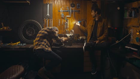 a guy mechanic together with his colleague work on a workbench and communicate in a cozy workshop with many tools