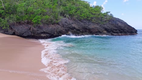 Pov-dolly-on-sandy-beach-of-Onda-with-splashing-clear-water-and-rocky-coastline-in-sunlight---No-people-on-tropical-spot-in-Dominican-Republic