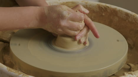 handheld close up shot of caucasian hands forming a vase with clay on a potter's wheel