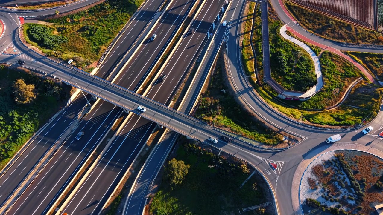 Highway overpass and dual roundabouts seen from above, Spain. Drone view of curving ramps, traffic and green median strips at golden hour.