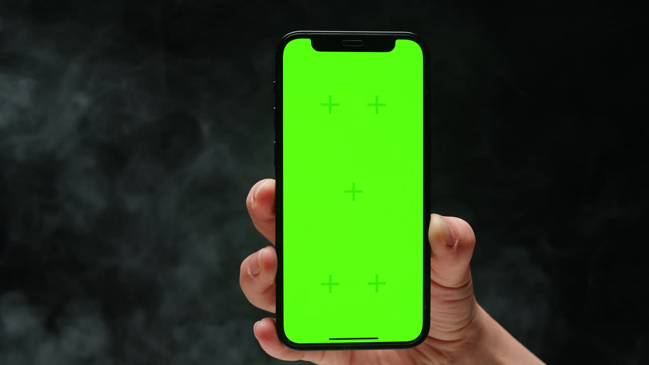 Smartphone with chroma key screen on black background close-up. Green screen on mobile phone in hand.