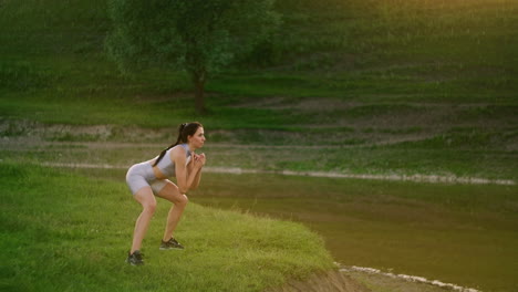una mujer hace ejercicios para los músculos de sus muslos y piernas en la hierba en un parque cerca del lago. trabaja con los músculos abdominales. figura delgada y hermosa. maratón de fitness
