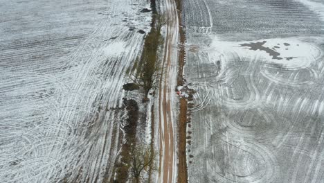 Siga-El-Camino-Aéreo-De-Grava-A-Lo-Largo-De-árboles-Y-Campos-De-Granos-Agrícolas-Cubiertos-De-Nieve