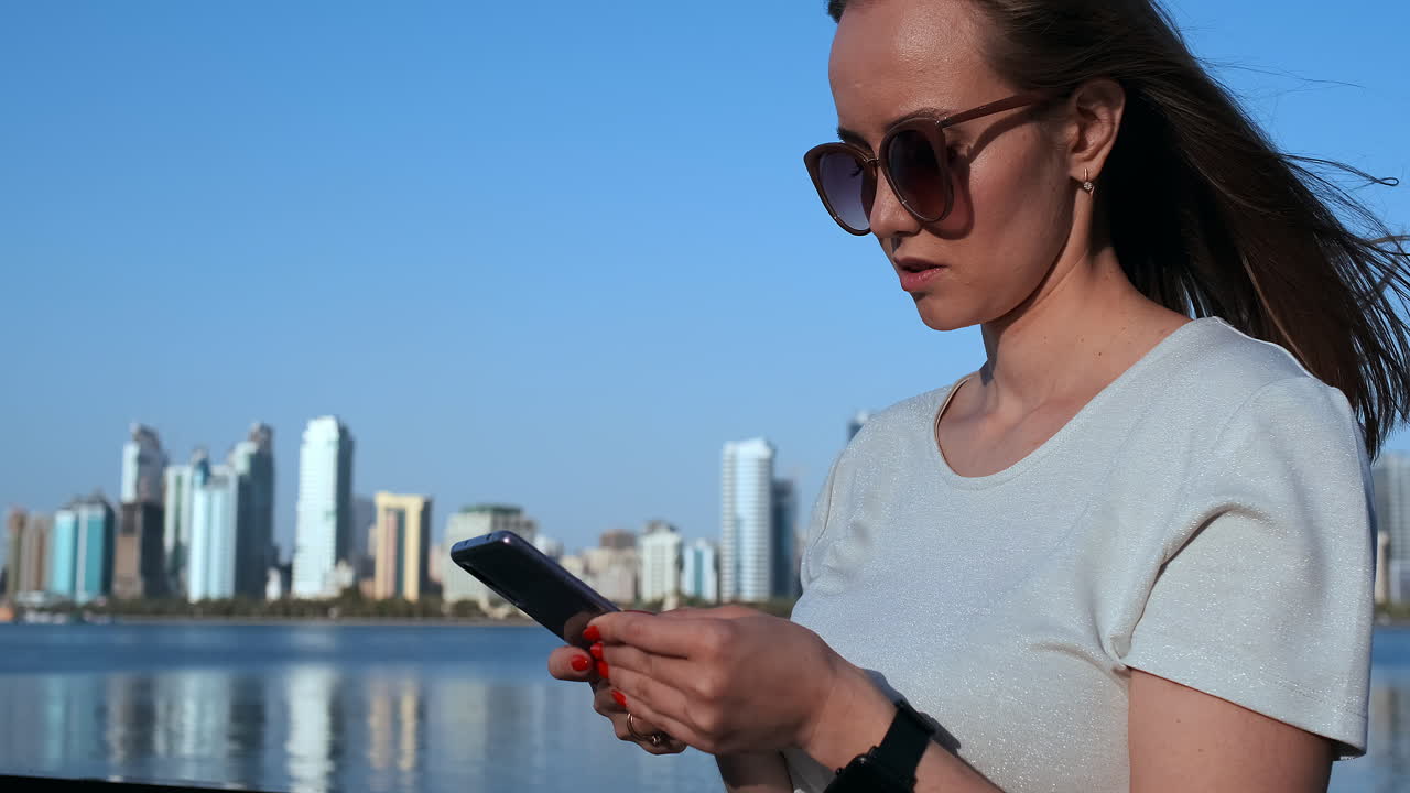 una chica con el pelo largo marca un mensaje en el teléfono inteligente en el muelle de dubai