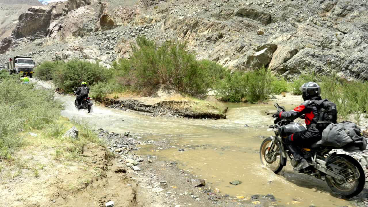 Bikers navigating a rocky desert trail crossing into water in Ladakh, India crossing vast arid landscapes on an adventurous ride