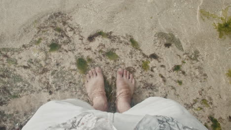 pov shot of feet standing on a beach in clear water and seaweed in bali,indonesia